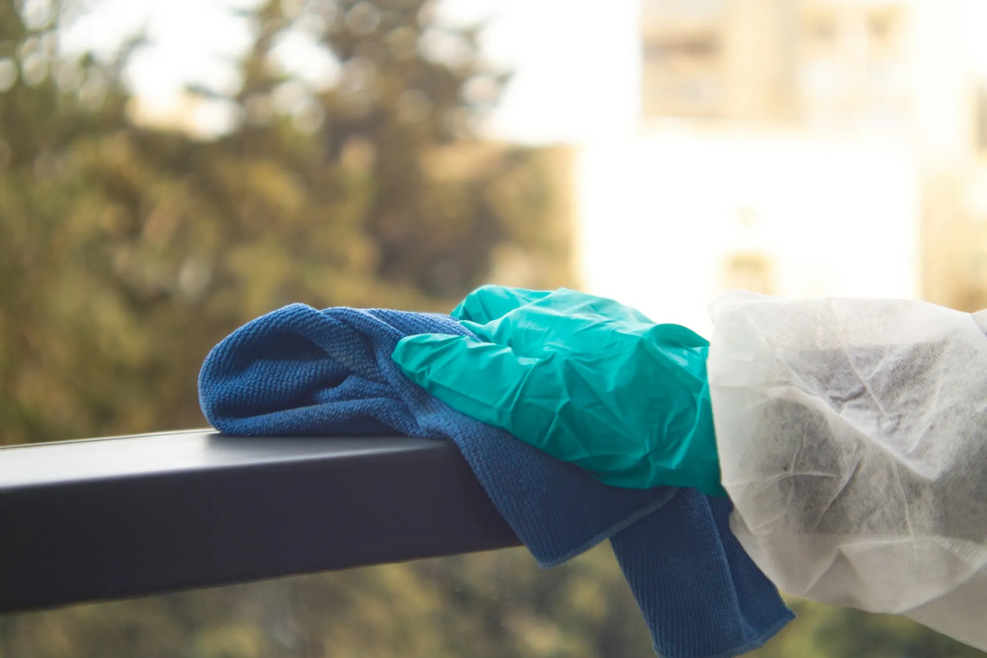 Gloved hand wiping a metal handrail with a blue cloth